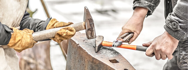A blacksmith man and his son forge a horseshoe on an anvil .Banner