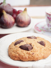 close-up chocolate chip biscuit with hijogs and cup of tea in the background out of focus