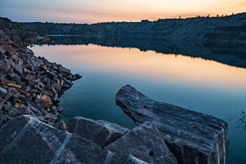 Old flooded stone quarry surrounded by stone waste from a mine work against a beautiful night sky