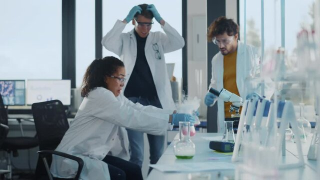 Medical Science University Laboratory Young Students Learning: Beautiful Black Scientist Mixes Chemical Liquid in two Beakers and Has Active Reaction, Her Colleagues Laugh and Cheer, Have Fun Together