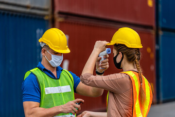 The foreman in a reflective safety vest and Yellow Helmet is checking the temperature with a thermometer. And spraying with alcohol to wash workers before entering work