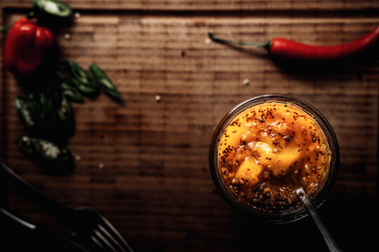 Mango Chutney in einem Glas und L&ouml;ffel auf einem Holzbrett stehend, im Hintergrund frischer Chili.