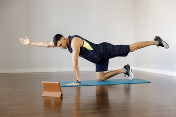 A young man in sportswear does a sports exercise. Online training. Stretching your hands and feet on the app in your phone. Healthy lifestyle in self-isolation