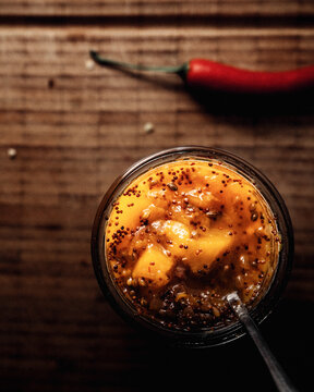 Mango Chutney in einem Glas und L&ouml;ffel auf einem Holzbrett stehend, im Hintergrund frischer Chili.