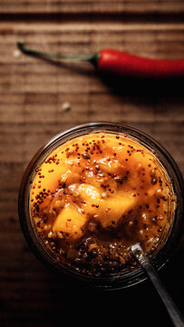 Mango Chutney in einem Glas und L&ouml;ffel auf einem Holzbrett stehend, im Hintergrund frischer Chili.