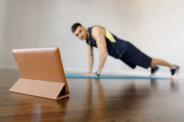 A young sports man does a plank exercise in self-isolation conditions. Online training at home with...