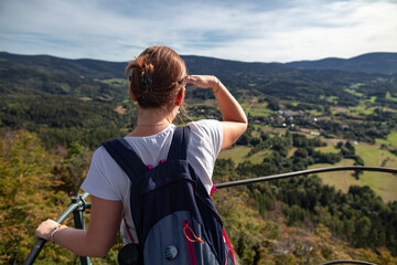 Turystka na szczycie Krzyżnej Góry przysłaniając słońce prawą dłonią wpatruje się w znajdujące się na horyzoncie Sudety, Rudawy Janowickie, Polska