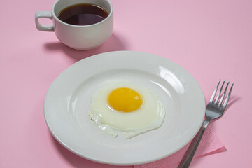 Scrambled eggs on a pink background. Fried eggs on a white plate. Delicious breakfast with a cup of coffee.