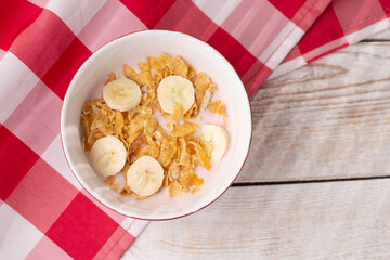 Healthy breakfast. Muesli with yogurt and banana on a light wooden background with a red tablecloth. View from above. Copy space.