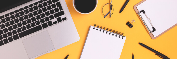 Banner with laptop and scattered stationery on a yellow background. Online business workspace, distance education, remote work concept.