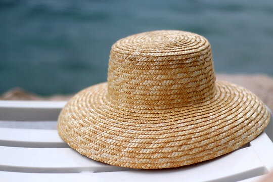 Straw hat on the deck chair by the water. Selective focus.