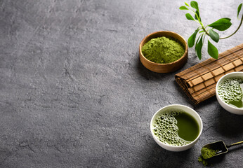 Matcha tea powder and tea accessories on dark background.