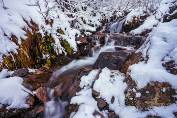 Small stream among wet stones and white snow in the picturesque Carpathian mountains in Ukraine