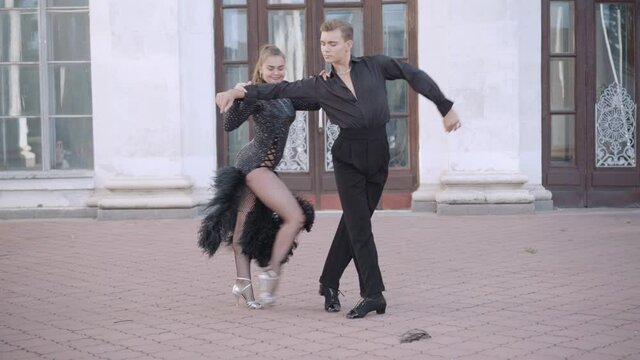 Wide shot of confident couple performing paso doble in urban city. Portrait of skilled talented young Caucasian ballet dancers dancing outdoors. Latin ballroom dancing.