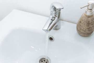 running clean water flows from the faucet in the bathroom in a white sink. plumbing