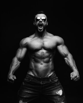 Screaming muscular male model in sunglasses on black background