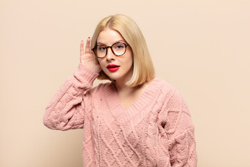 blonde woman looking serious and curious, listening, trying to hear a secret conversation or...