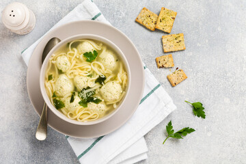 Bowl of traditional Italian soup with chicken meatballs and egg paste, Parmesan cheese, parsley on gray table background. Traditional Italian kitchen. Top view.