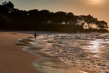 Woman is walking alone on a beach during sunset.