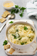Bowl of traditional Italian soup with chicken meatballs and egg paste, Parmesan cheese, parsley on gray table background. Traditional Italian kitchen. Top view.