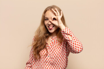 blonde woman smiling happily with funny face, joking and looking through peephole, spying on secrets