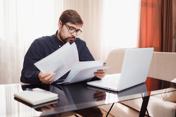 Entrepreneur works with a laptop and keeps a document in a home office