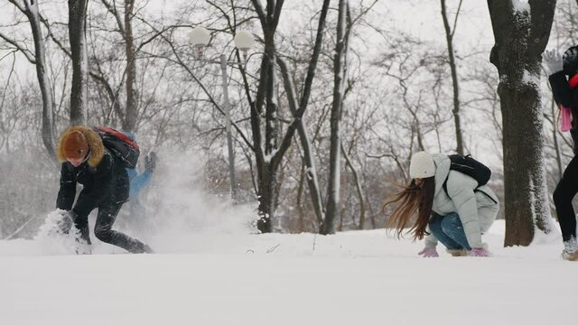 Children enjoy the first snow in the park in winter. Teenagers with backpacks are playing funny throwing snow at each other. Fun outdoor activities for schoolchildren