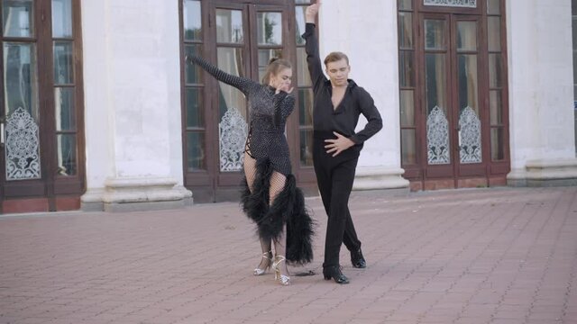 Wide shot of professional dancers dancing paso doble in urban city. Portrait of confident Caucasian young man and woman performing latin ballroom dance outdoors walking to each other.