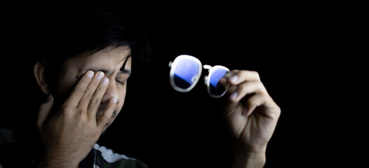 Asian Man rubbing tired eyes. Problem with glasses, eyesight or vision Working with computer at...