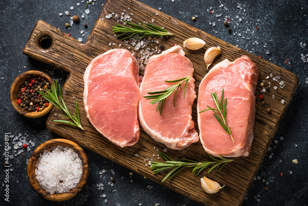 Wall mural Pork meat. Fresh pork steaks on cutting board with ingredients for cooking. Top view at black stone table.