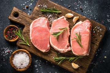 Pork meat. Fresh pork steaks on cutting board with ingredients for cooking. Top view at black stone...