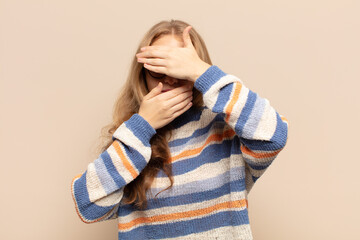 blonde woman covering face with both hands saying no to the camera! refusing pictures or forbidding...