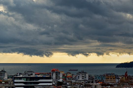 Dramatic landscape of stormy sky over small seaside city. The sky turned yellow before the storm. Dark nimbostratus clouds hang over town and sea. Weather forecast and meteorology.