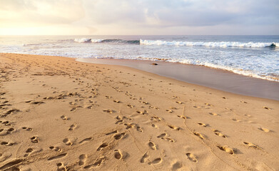 Sandy tropical beach with many footprints at sunset.