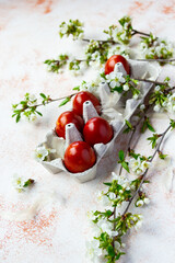 Red Easter eggs with spring flowered brunches on the light beige background. Vertical shot
