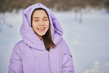 an emotional female in a purple down jacket enjoys the snow in the park