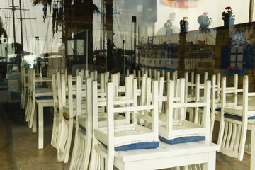 Chairs piled on tables in a closed cafe. Reflection of the resort embankment in the glass of the cafe. Lockdown, quarantine.