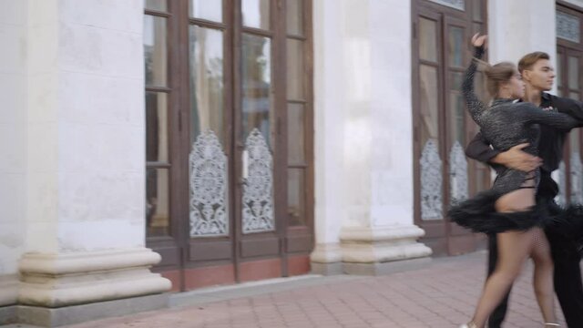 Live camera follows talented young couple of dancers performing latin ballroom dance in urban city. Wide shot of skilled Caucasian man and woman dancing outdoors. Choreography art concept.