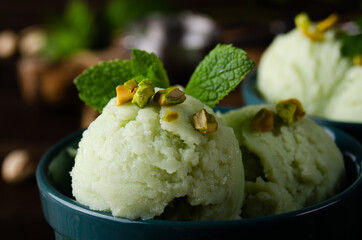 Pistachio icecream balls in clay bowls on wooden kitchen table with crumbs and nuts aside