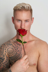 Male lover hiding behind a flower / Handsome young man holding a red rose in front of his face