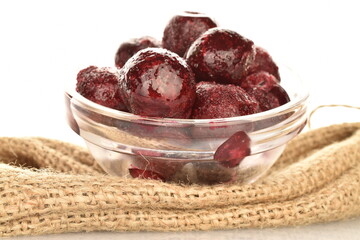 Several sweet organic pitted frozen red cherries in a glass dish on a burlap, close-up, isolated on white.