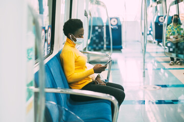 A young African woman in a protective mask rides the subway and listens to music with headphones....