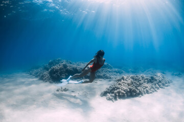 Woman freediver in red swimsuit with white fins posing underwater in tropical ocean. Sporty girl dive underwater.