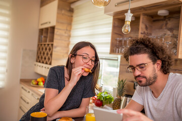 Couple sitting at kitchen counter, having breakfast and reading news