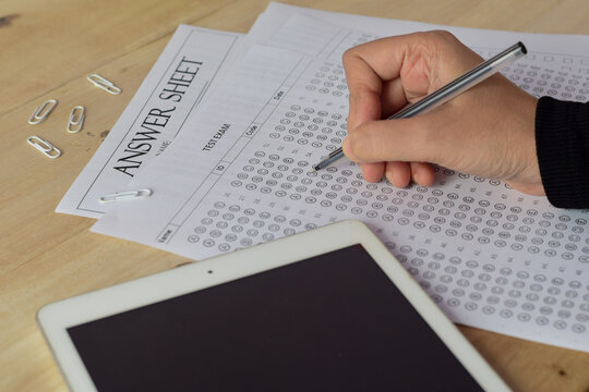 Student practicing answer sheets for the preparation of multiple choice questions MCQ exam on wooden table. Concept of mock and practice test, selective focus.
