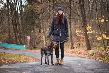 serious natural girl with brown hair with her dog Bohemian Wire-haired Pointing Griffon breed is walking through nature. Candid portrait of young woman with man's best friend. Binary portrait nature