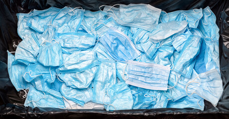 Discarded medical waste mask on virus banner in garbage can. Contaminated used trash disposable...