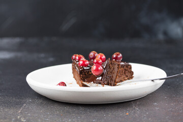 A broken piece of gluten-free Brownie chocolate cake, without eggs, on a white plate, on a dark background.
