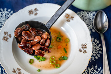 Ladle in plate with big bean soup, pot, spoon and pot.