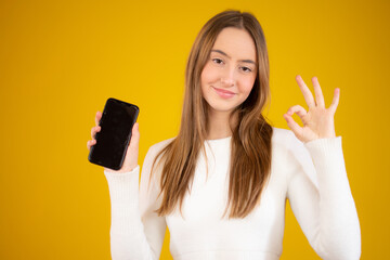 Smiling business woman showing blank smartphone screen over yellow background